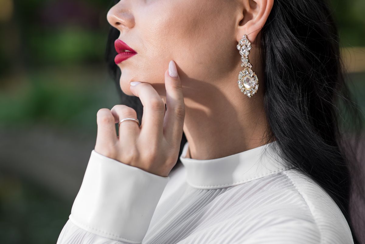 An elegant Caucasian brunette woman has an earring on the ear. Close up of bijouterie. Fashion concept