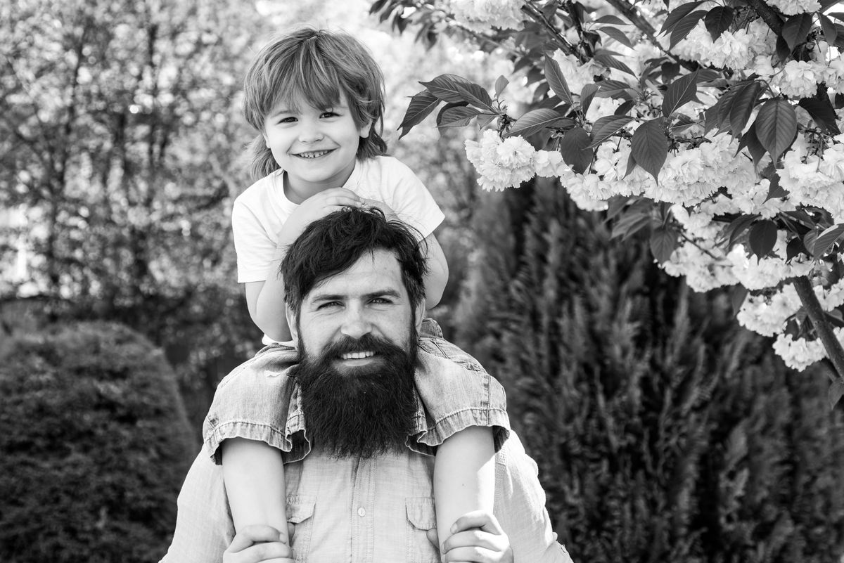 Father and son. Happy father giving shoulder ride on his shoulders in garden. Cute boy sitting on father's shoulders